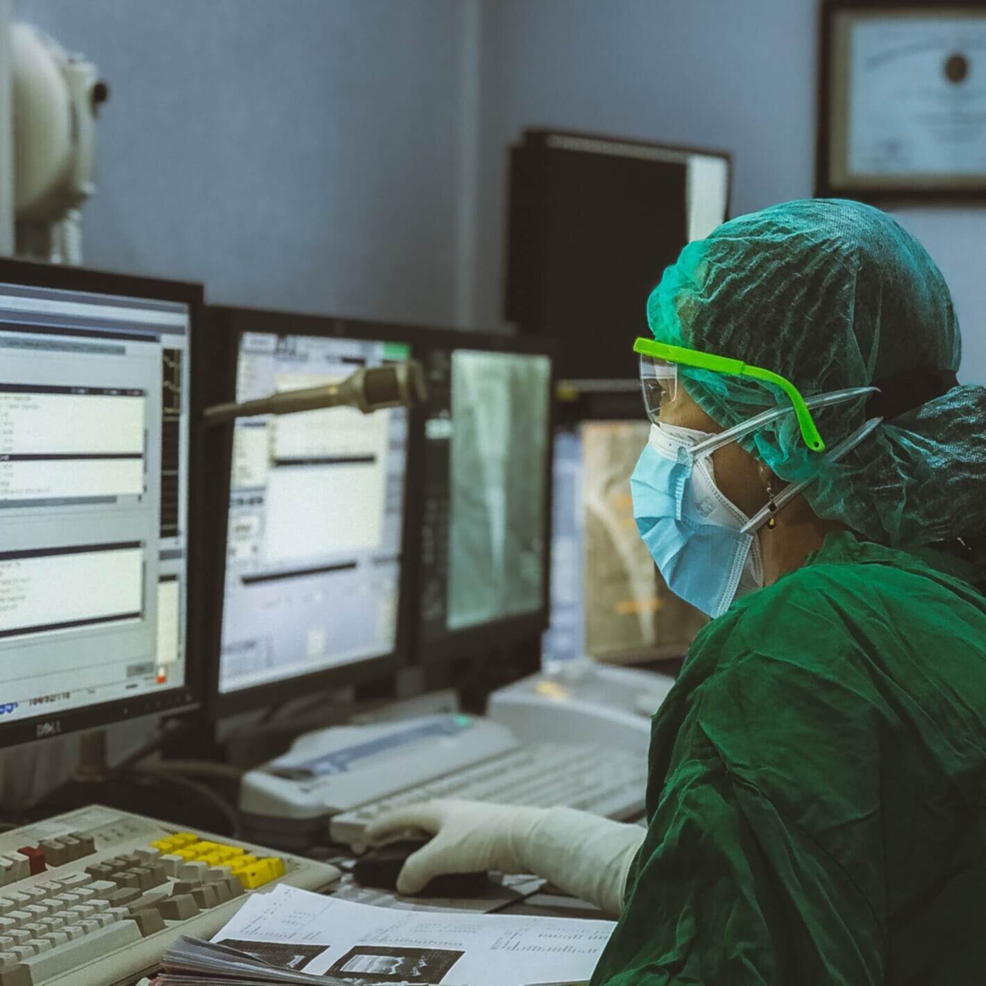 Person with hairnet, mask and scrubs on looking at computer screen