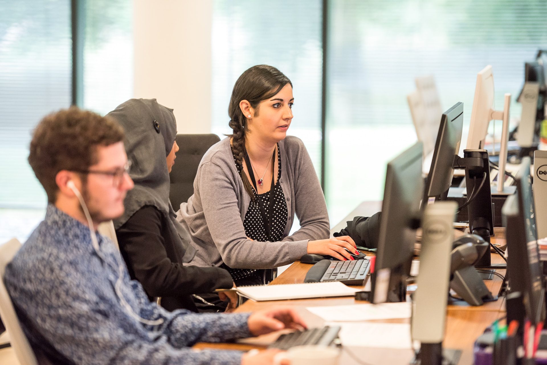 Two women working together next to a man working on his computer.