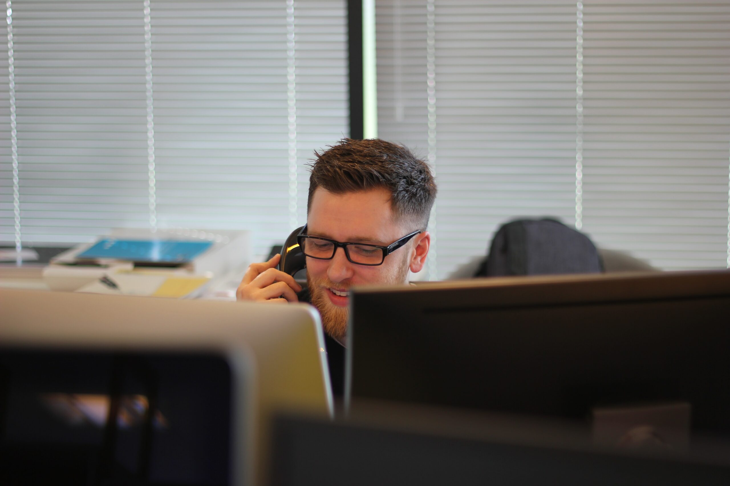 Man with glasses sat at desk, holding telephone